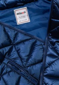 Navyblaue, gesteppten Pufferjacke mit glänzender Textur im Inneren, ausgestattet mit einem Reißverschluss und einem Markenetikett, das die Größe 8-9 Jahre angibt.