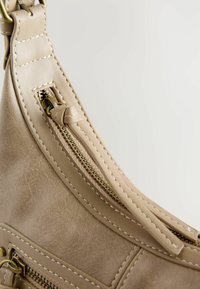 Borsa in finta pelle beige con una superficie liscia, dotata di chiusura con zip e cuciture dettagliate lungo i bordi. Finitura in hardware color oro.