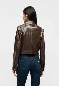 Καφέ cropped μπουφάν από τεχνητό δέρμα με γιακά και μακριά μανίκια. Ομαλή υφή, με μια μόνο ραφή που τρέχει στο κέντρο της πλάτης.