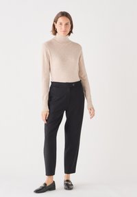 Lichtbeige coltrui, zachte textuur, gecombineerd met zwarte high-waisted broek, gladde stof, met een knoopaccent en taps toelopende pijpen.