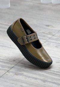 Ruskea kumikenkä kiiltävällä pinnalla, Mary Jane -tyyliä, jossa on musta uritettu pohja ja hihna, jossa on hopeisia niittejä.