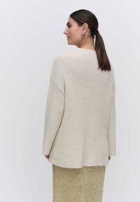 Kremowy sweter o prążkowanej strukturze z długimi rękawami, luźnym krojem i opadającymi ramionami, w połączeniu ze skrzącą się złotą spódnicą wyszywaną cekinami.