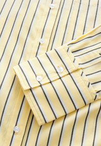 Manche de chemise jaune et panneau avant avec des rayures verticales noires et blanches et des boutons blancs en gros plan.