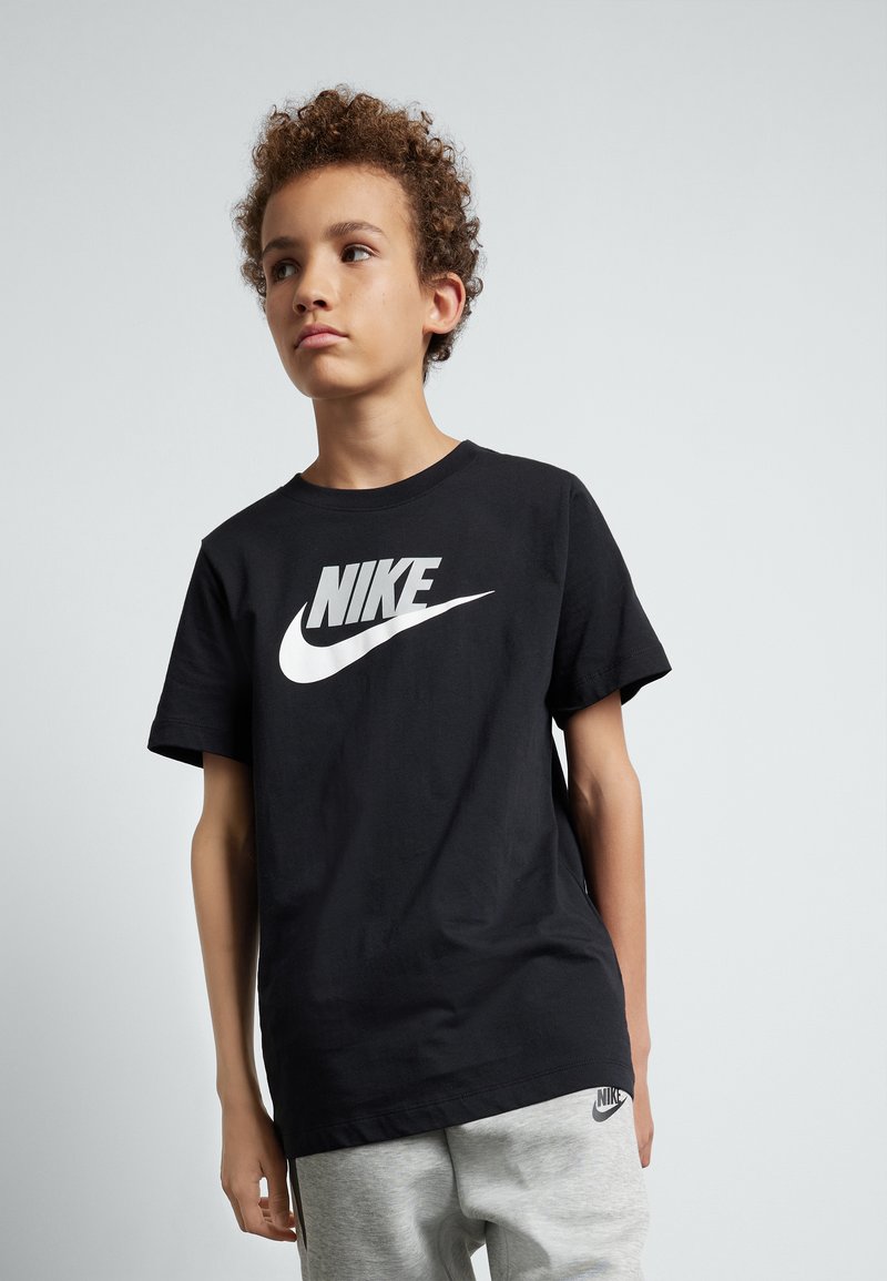 Camiseta de algodón negra con el logo blanco de Nike en el frente. Diseño de mangas cortas y cuello redondo. Combinada con pantalones de chándal grises con detalles del logo.