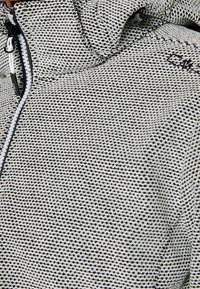 Texturierte Jacke mit einem Schwarz-Weiß-Muster, ausgestattet mit einem Reißverschluss und einer Kapuze. Der Stoff wirkt dick und hat eine strickähnliche Qualität.