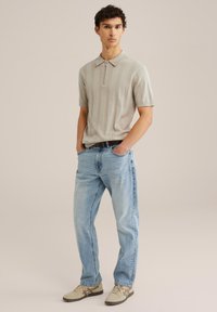 Polo corto de color gris claro con rayas verticales, cremallera plateada, combinado con jeans de mezclilla azules y zapatillas beige con detalles marrones.
