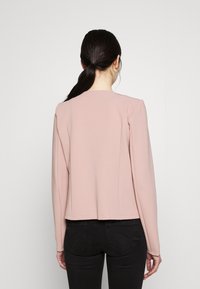 Haut ajusté à manches longues, de couleur rose clair, col rond, texture lisse, légèrement extensible, avec un ourlet droit et sans fermetures visibles.