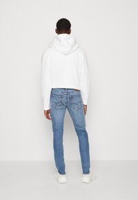 Sudadera blanca acortada con capucha, combinada con unos vaqueros de mezclilla azul claro que cuentan con bolsillos traseros y un sutil bordado. Incluye zapatillas blancas.