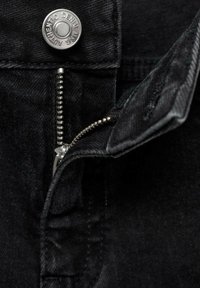 Črn denim material v bližnjem posnetku, ki prikazuje srebrno zadrgo in gumb, z natančnim šivanjem in teksturirano notranjostjo.