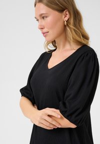 Black textured top with a V-neckline and puffed short sleeves. Fabric appears lightweight. Simple design with no patterns or accents.