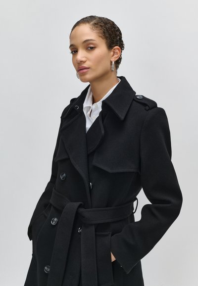 Juodas vilnonis paltas su dvigubos krūtinės dizainu, dideliu koloriumi, dirželiu juosmens srityje ir šoninėmis kišenėmis. Tekstūruotas audinys su mygtukais ir epauletais.