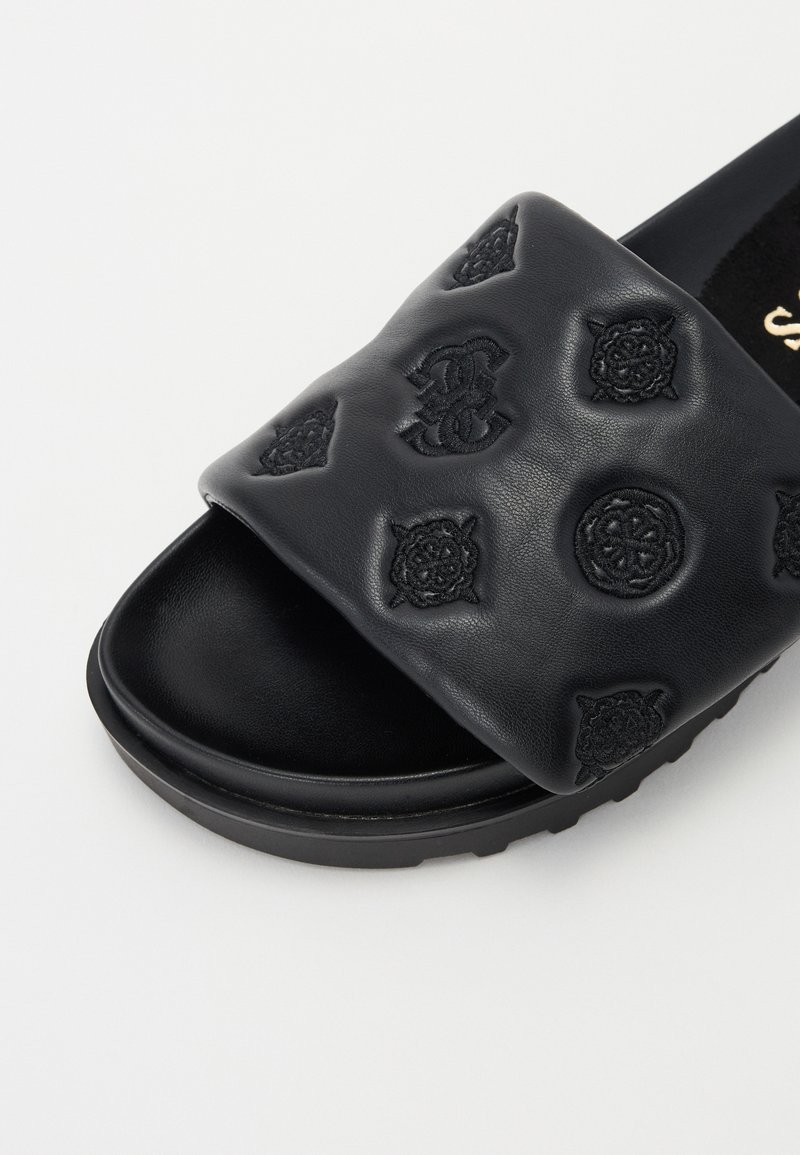 Sandale à glissière en cuir noir avec une sangle rembourrée ornée de motifs en relief et une semelle intérieure texturée, reposant sur une semelle extérieure noire robuste.