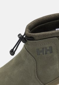 Green suede ankle boot with a textured fabric collar, drawcord closure, and black logo detail on the side. Features a smooth, solid sole.