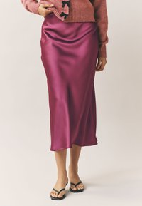 Satenasti magenta midi krilo z gladko teksturo in širjenjem na dnu, v kombinaciji s črnimi natikači.