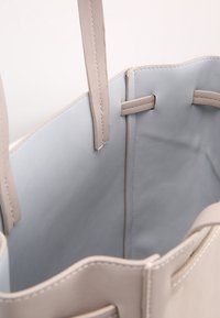 Beżowa skórzana torba na ramię z miękkim szarym wnętrzem, podwójnymi uchwytami i prostymi krawędziami. Wyłożona gładkim materiałem, idealna do codziennego użytku.