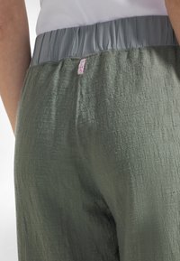Lekkie oliwkowozielone spodnie o fakturowanej powierzchni z elastycznym, szarym pasem, z małą różową metką z tyłu.
