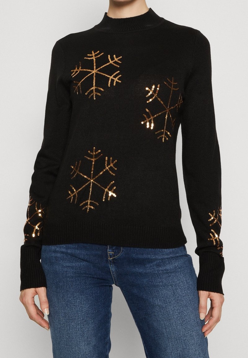 Pull noir en tricot avec manches longues, décoré de flocons de neige métalliques dorés sur le devant et les manches. Col et poignets côtelés.