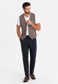 Brązowa kamizelka w kratę na białej koszulce, w połączeniu z ciemnymi spodniami i brązowymi butami z wiązaniem. Casualowy, ale schludny wygląd.