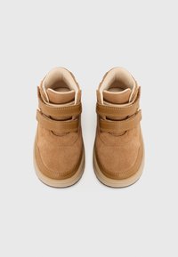Bottes montantes en suède marron avec deux bandes Velcro, intérieur en crème doux et semelle en caoutchouc, avec un design à bout arrondi.