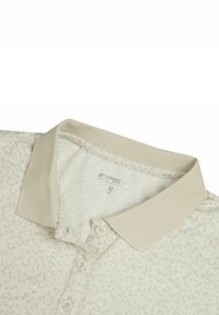 Jasnobeżowa koszulka polo z delikatnym wzorem liści, prążkowanym kołnierzykiem i listwą na trzy guziki. Metka wskazuje rozmiar M. Miękka w dotyku tkanina.