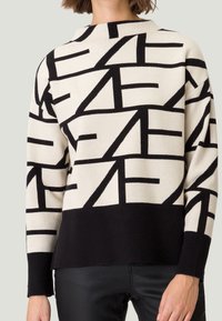 Gebreide trui in crèmekleur met zwart geometrisch patroon, voorzien van een ronde hals en geribde zoom. Lange mouwen met een losse pasvorm.