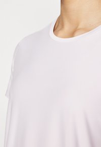 Maglietta a maniche corte rosa chiaro con scollo rotondo, realizzata in tessuto morbido. I dettagli delle cuciture sono visibili vicino al collo e alla spalla.
