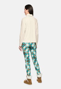 Beige long-sleeve top with a high collar, paired with multicolored plaid leggings in teal, brown, and orange. Brown boots with white fur accents.