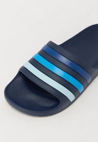 Navy blue slide sandal made of textured rubber, featuring three horizontal stripes in dark blue, light blue, and pale blue across the upper.