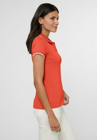 Korte mouwen polo-shirt in feloranje katoen. Kenmerkt zich door een klassieke kraag, twee knopen en witte afwerking langs de kraag en mouwen.