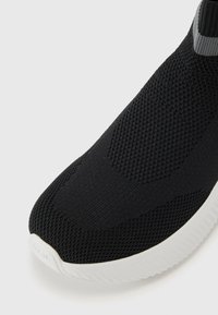 Black athletic shoe featuring a sleek, knit upper with a textured pattern, complemented by a white rubber sole and grey accent on the collar.