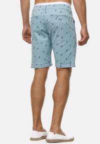Mint green shorts featuring a repeated palm tree pattern, made from lightweight fabric, with side pockets and a rolled hem.