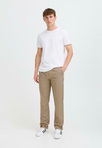 White short-sleeve t-shirt, beige pants with a textured pattern, and white sneakers with black stripes. Model stands confidently.