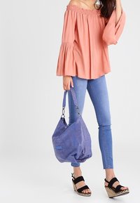 Haut rose dénudé d'épaules avec des manches évasées, jean skinny bleu, sandales à plateforme noires et un sac à main texturé violet.