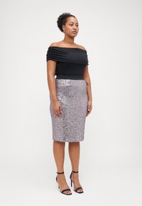 Melnā blūze bez piedurknēm ar savilktu audumu, apvienota ar pieguļošiem lavandas krāsas spīdīgu svārku. Melni sandalītes ar augstu papēdi un siksniņām.