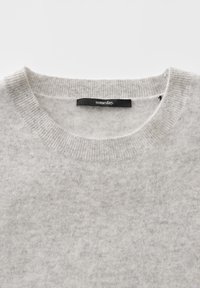 Pull léger gris clair avec une texture de tissu douce et une étiquette noire portant l'inscription "someday" cousue à l'intérieur du col.