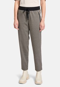 Pantalons à carreaux noir et blanc avec une taille élastique noire, dotés d'un cordon de serrage et de poches zippées sur les côtés. Texture de tissu lisse.