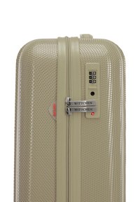 Maleta rígida en color beige claro, con textura en panal, doble cremallera, cerradura de combinación y etiquetas de marca para mayor seguridad.