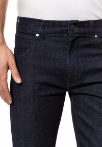 Ciemnoniebieskie dżinsy o prostym kroju, z zapięciem na guzik i zamek błyskawiczny, klasyczny pięciokomorowy design i widoczna struktura materiału.