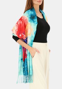 Kolorowy szal w kwiatowy wzór wykonany z lekkiego materiału, zawierający odcienie niebieskiego, czerwonego i pomarańczowego, z frędzlami wzdłuż krawędzi.