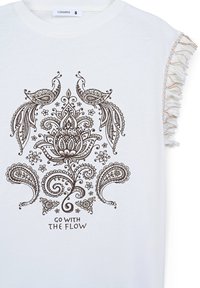 Maglietta in cotone bianco con dettagli a frange, caratterizzata da un design paisley marrone e floreale con il testo "VAI CON IL FLUSSO" in basso.
