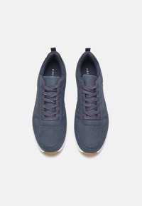 Granatowe buty sportowe z gładką syntetyczną cholewką, okrągłym czubkiem, sześcioma oczkami na sznurówki oraz białą gumową podeszwą. Obecne detale teksturowane.