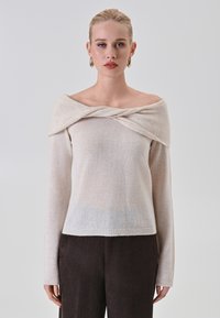 Maglione off-the-shoulder in maglia color crema, con un collo torcigato e maniche lunghe. Orlo a costine e materiale morbido e testurizzato.