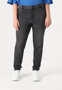 Black denim jeans with a slim fit, five pockets, and a zipper fly. Worn with white sneakers and a blue top, showcasing a casual style.