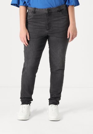 Black denim jeans with a slim fit, five pockets, and a zipper fly. Worn with white sneakers and a blue top, showcasing a casual style.