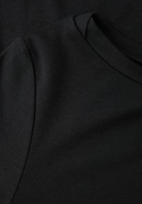 Schwarze Baumwoll-T-Shirts, die übereinanderliegen, mit einer glatten Textur, Rundhalsausschnitt und kurzen Ärmeln. Der Stoff wirkt weich und flexibel.