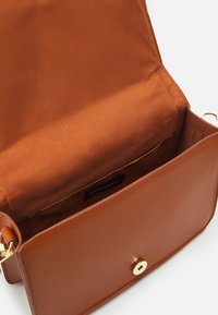 Bruine leren handtas met een gladde textuur, gouden hardware en één vak. Het interieur heeft een satijnen voering en een klein zakje.