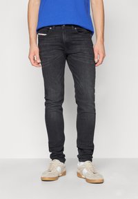 Fekete, slim fit farmernadrág, öt zsebbel, kontrasztos varrással, világos színű sportcipővel viselve.