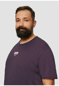 Paarse korte mouwen T-shirt met een ronde hals en een klein crèmekleurig label met logo op de borst. Zachte, gladde stoftextuur.