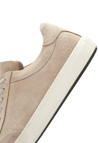 Zapatillas de ante beige con punta redonda, suela de goma blanca y cordones grises. Presentan detalles de costura en la parte superior y en el talón.