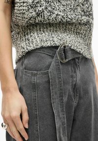 Grå jeansbyxor med vid midja och skärp. Har två sidofickor och en mjuk, strukturerad stickad tröja med monokromt mönster.